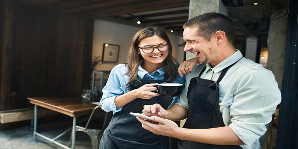 Café staff smiling while viewing a phone, symbolizing the shift from traditional tiered models to engaging badge-based loyalty programs.
