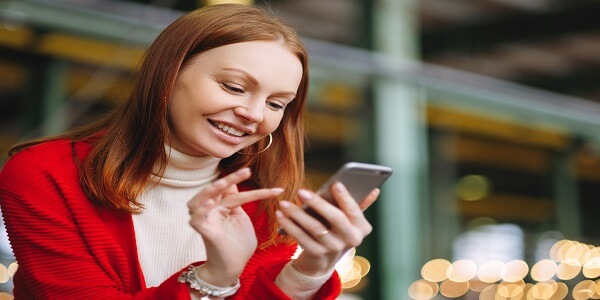 Smiling woman using her phone, illustrating how AI-powered SMS and email solutions help brands drive repeat sales.