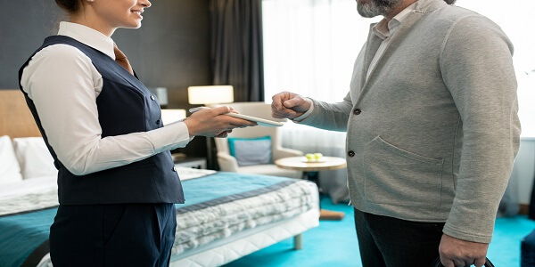 Hotel staff assisting a guest with a digital tablet, showing ways to enhance and make a hotel reward program more competitive.