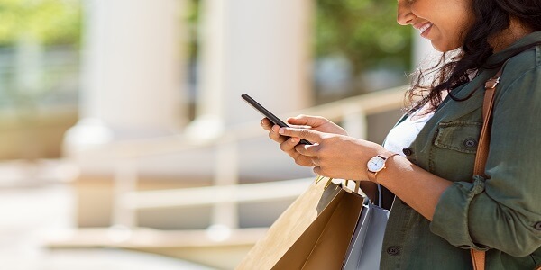 Shopper checking her phone while carrying bags, reflecting how omnichannel retail programs influence the future of POS systems.