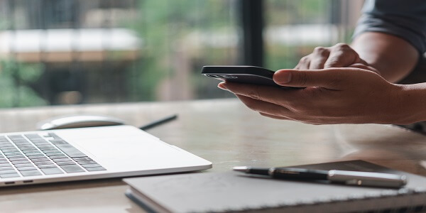 Person using phone and laptop to plan BFCM SMS and emails