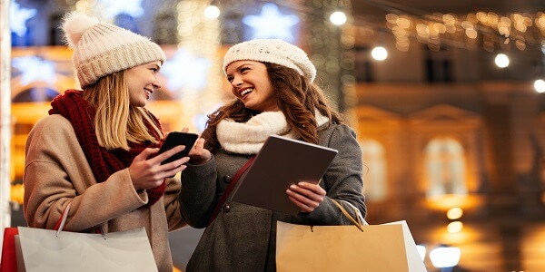 Two friends holiday shopping and using digital devices, showing how loyalty programs build lasting connections during Christmas.