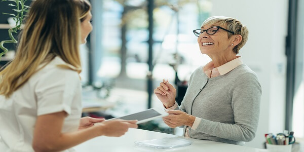 Senior woman getting friendly support at a healthcare desk, showing how loyalty programs improve patient experience and benefits in 2024.