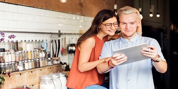 Young couple in a cozy store-kitchen environment using a digital tablet, representing how phygital commerce blends in-store experiences with digital engagement to build customer loyalty.