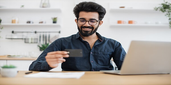 Man holding a payment card and using a laptop, illustrating digital payments and Visa’s new Web3-driven loyalty solution.