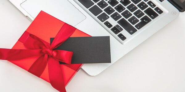 Red gift box and black digital gift card on a laptop, symbolizing the rise of online gift cards as the future of gifting.
