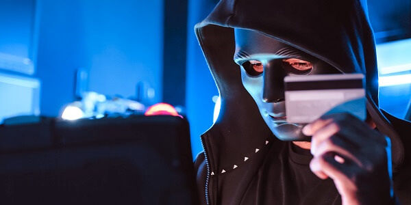 Masked hacker holding a credit card in front of a laptop, symbolizing cybersecurity threats in loyalty programs.