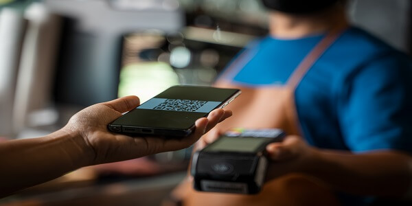 Close-up of a hand holding a smartphone near a payment terminal, representing mobile wallet payment and loyalty reward redemption.